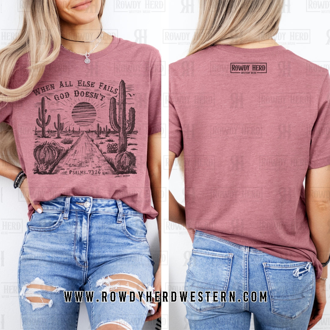 Soft heather mauve Bella + Canvas unisex t-shirt featuring a sublimation desert scene with the faith-inspired quote "When All Else Fails, God Doesn’t" at the top and "Psalms 73:26" at the bottom. A stylish and meaningful Christian apparel piece with a Western touch.