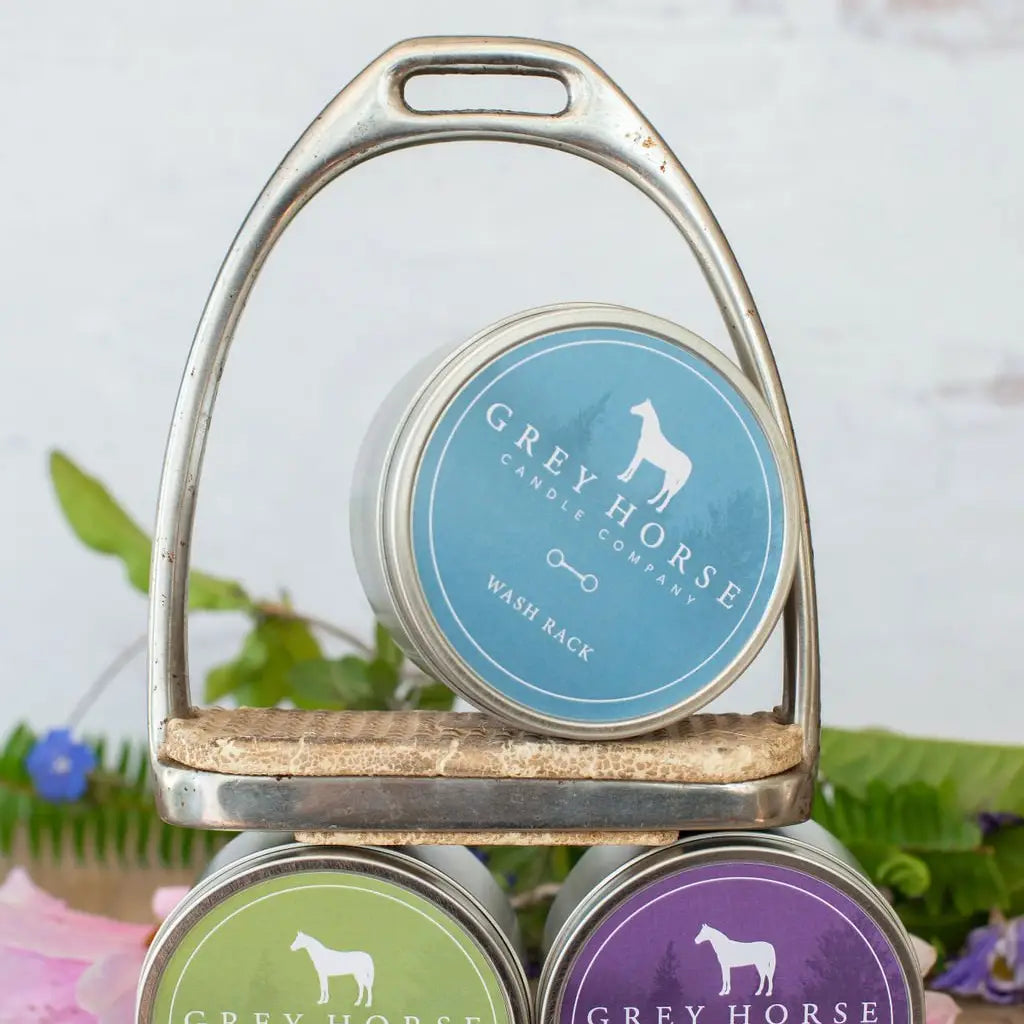 Wash Rack scented 6.3 ounce candle tin sitting on a horse stirrup.