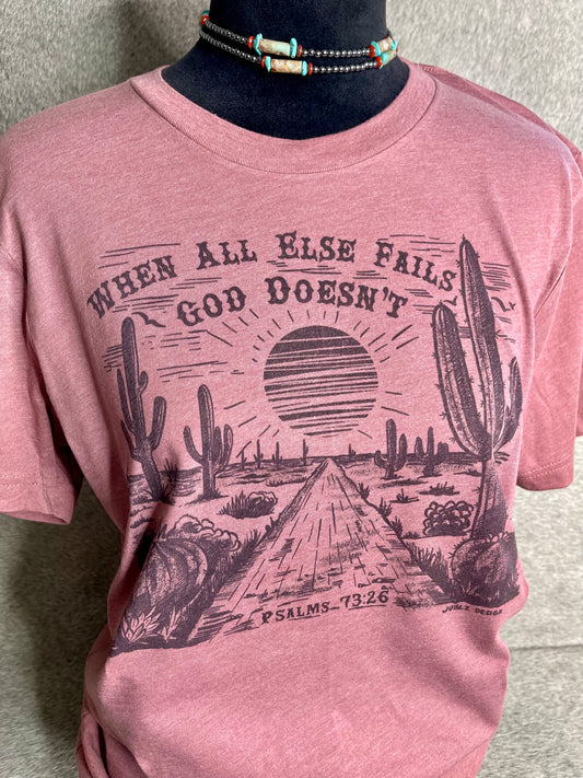 Soft heather mauve Bella + Canvas unisex t-shirt featuring a sublimation desert scene with the faith-inspired quote "When All Else Fails, God Doesn’t" at the top and "Psalms 73:26" at the bottom. A stylish and meaningful Christian apparel piece with a Western touch.