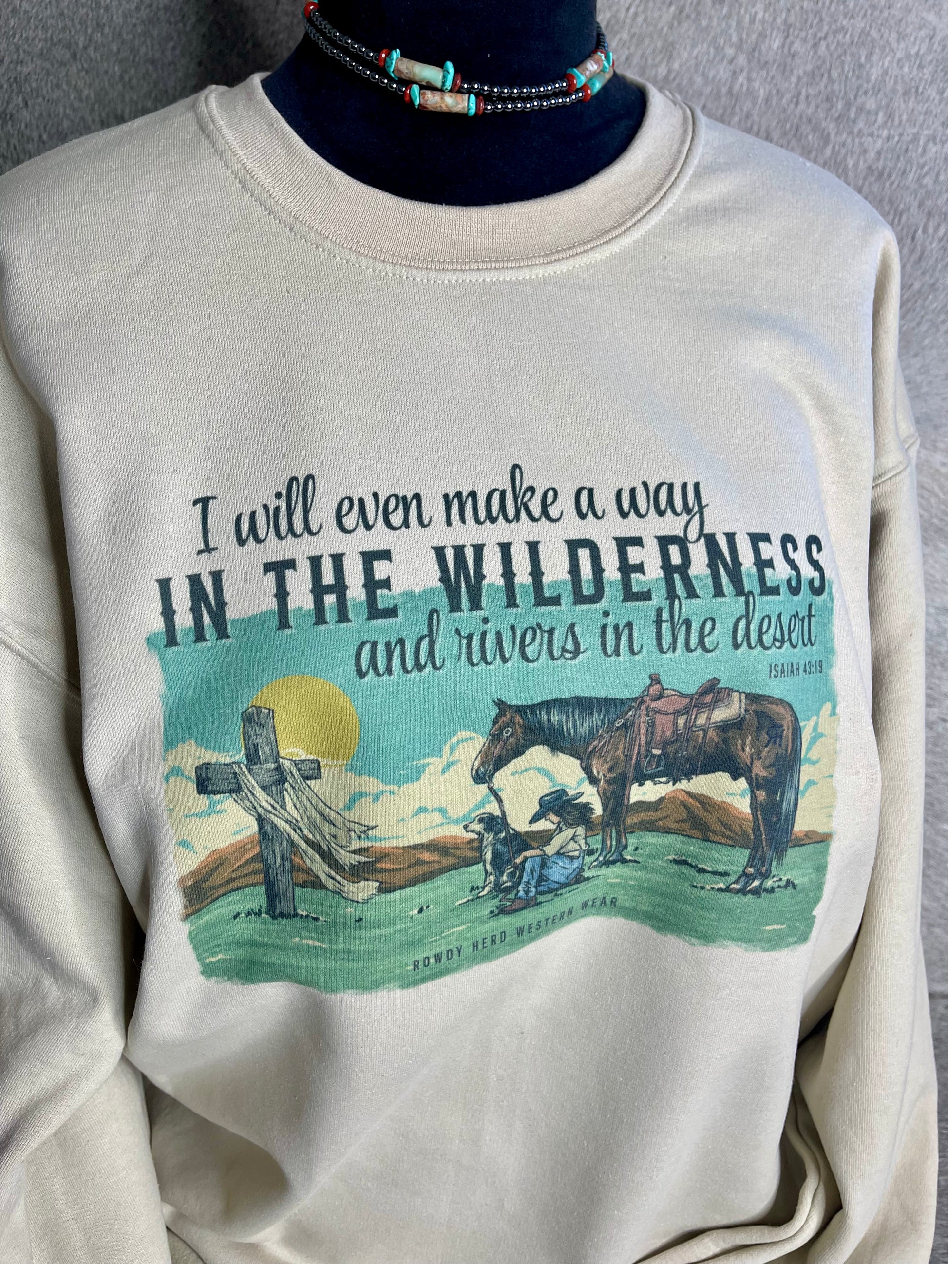 Unisex Gildan sweatshirt in sand with a vibrant design of a praying cowgirl, her dog, and horse, quoting Isaiah 43:19.