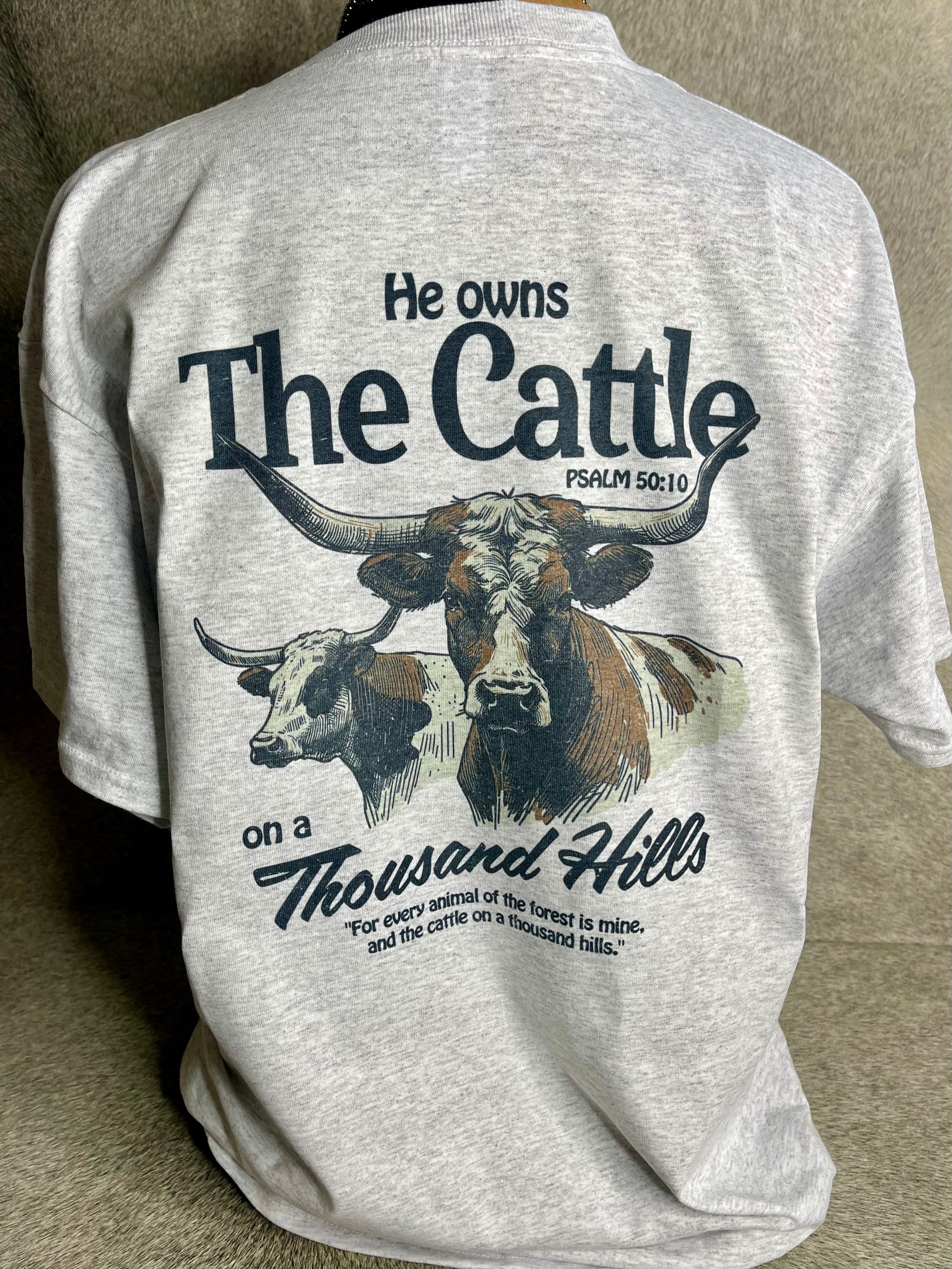 A stylish heather grey Jerzees unisex t-shirt with the Rowdy Herd logo on the front pocket and a detailed longhorn cattle design on the back, featuring the inspirational Psalms 50:10 verse