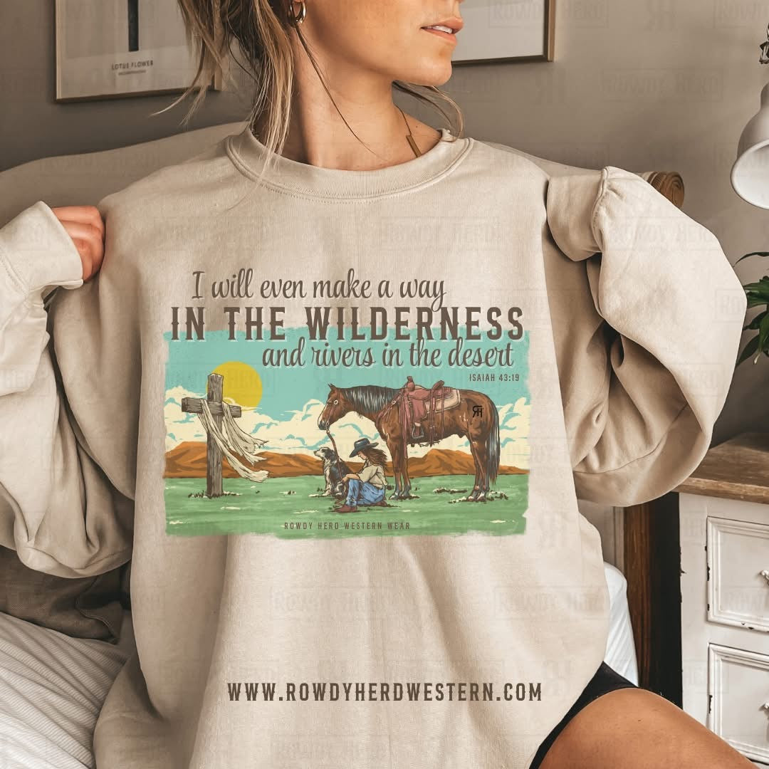 A mockup of our unisex Gildan sweatshirt in sand color featuring a sublimated design of a praying cowgirl with her dog and horse, along with the Isaiah 43:19 quote