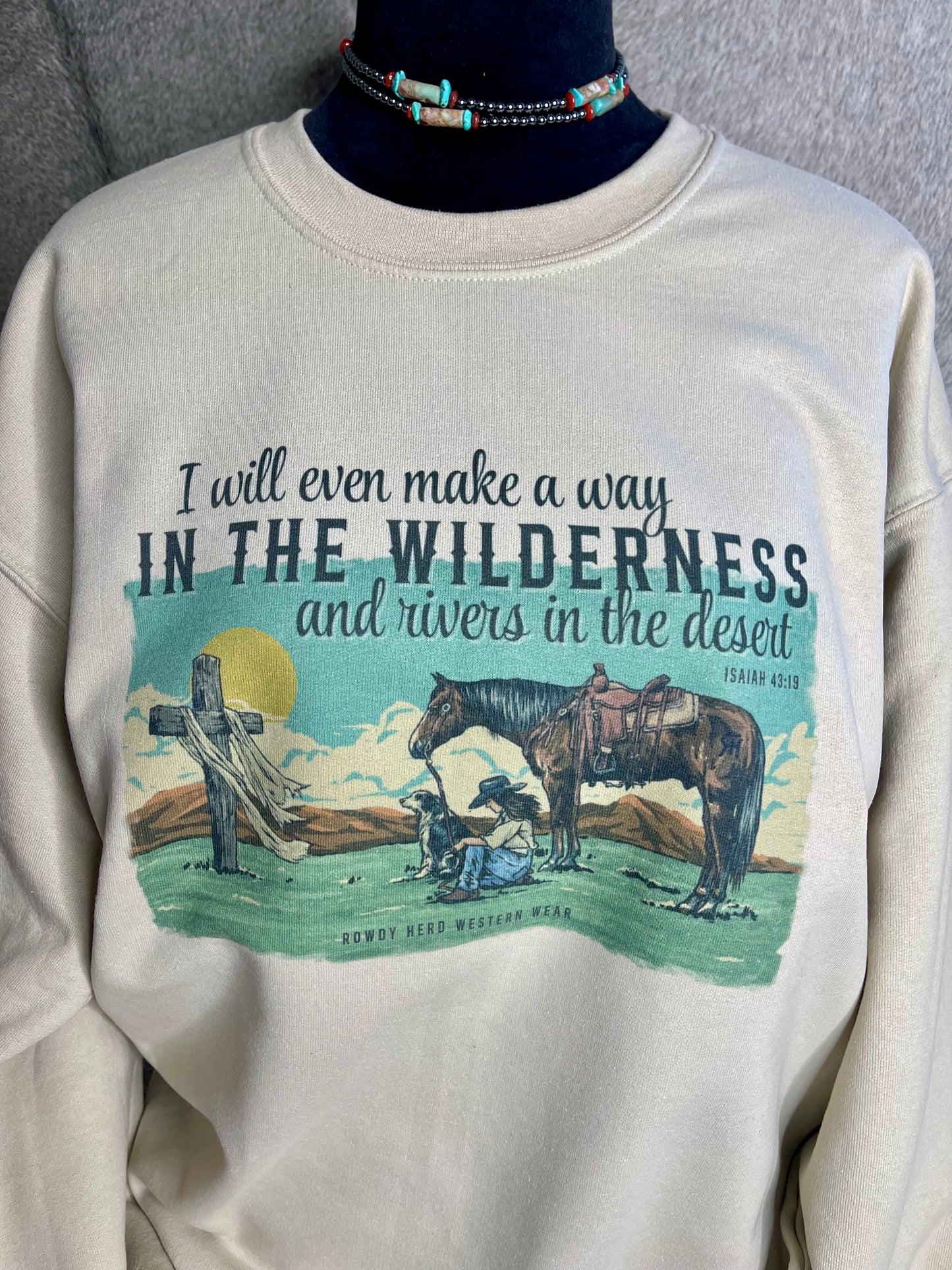 Gildan unisex sweatshirt in sand, featuring a stunning design of a praying cowgirl surrounded by her dog and horse, with Isaiah 43:19 elegantly quoted